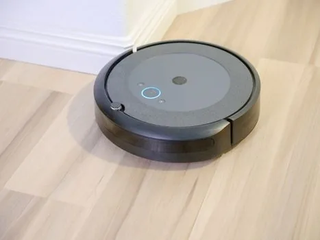 a close-up of a robot vacuum cleaning pet hair and dust off a light wooden floor next to a sofa leg, soft natural light, editorial lifestyle photography, shallow depth of field, no people