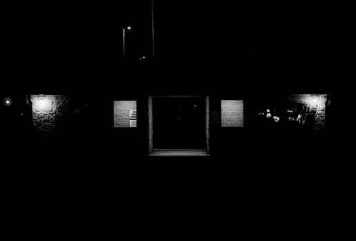 a dark cinematic movie scene playing on a television in a dimly lit living room at night, deep blacks on screen, soft ambient glow, editorial photography, no text