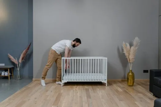 a natural evaporative humidifier with a wet filter standing quietly beside a crib in a soft bright nursery, gentle daylight, safe calm atmosphere, editorial interior photography, no people, no text