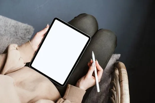 a person holding a large screen tablet showing a handwriting note app with a stylus, hands only, cozy living room background blurred, soft lamp light, editorial lifestyle photography, no face