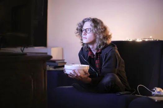 a person sitting on a sofa watching a large television across a living room, measuring tape on the floor showing distance, daytime soft light, wide shot, editorial photography, no face close-up