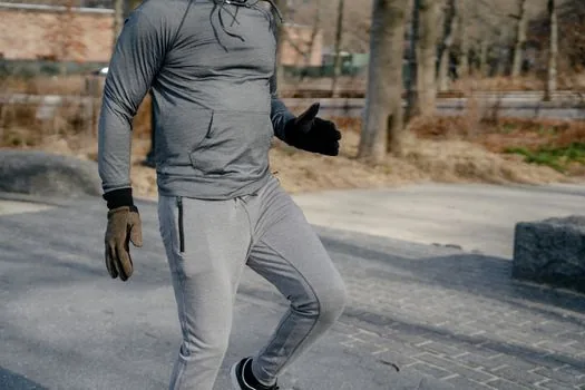 a person wearing wireless earbuds while jogging on a city street at sunrise, seen from behind, motion blur in the background, warm golden light, editorial lifestyle photography, no face visible