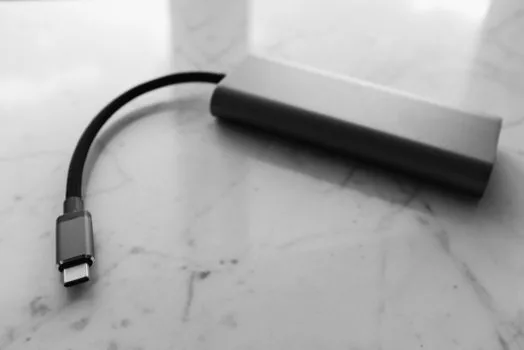 a small white gan usb-c wall charger plugged into a power strip next to a laptop and a tablet on a clean desk, soft daylight, close-up product photography, shallow depth of field, no people