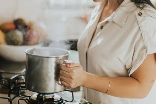 a steel pot of water boiling on a black induction cooktop in a bright modern kitchen, steam rising, close-up side view, editorial product photography, shallow depth of field
