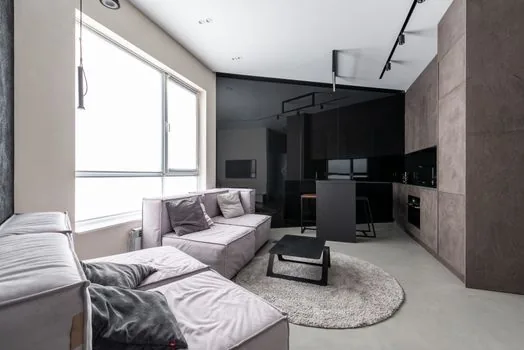 an open-plan Korean apartment living room connected to a kitchen, bright natural daylight through large windows, clean modern interior, wide shot, editorial interior photography, no people