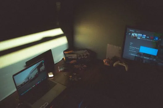 two gaming monitors of different sizes side by side on a desk showing a detailed game landscape, comparing screen real estate, soft studio light, editorial product photography, no people