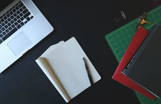 two thin laptops stacked on a minimalist desk next to a notebook and pen, lifestyle product photography, natural daylight