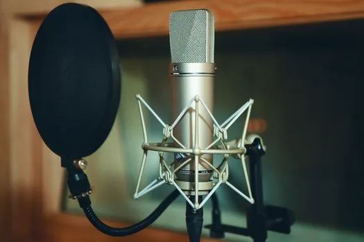 a black usb condenser microphone with a metal pop filter on a boom arm over a desk, warm key light, shallow depth of field, editorial product photography