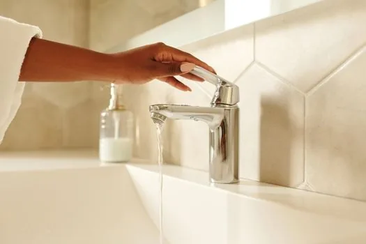 a person's hand pulling out the full water tank from a home dehumidifier, water visible inside, bright bathroom in background, lifestyle photography