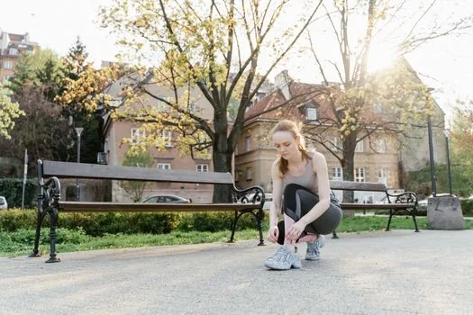 a person tying running shoes outdoors wearing a sports smartwatch on wrist, early morning park, no face closeup, editorial photography