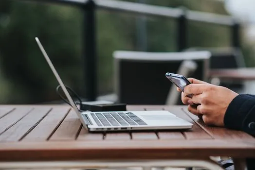 hand placing generic wireless earbuds into pairing mode beside smartphone and laptop, soft daylight, no brand, no text