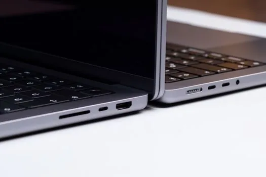 two laptops of different sizes side by side on a table comparing thickness, natural daylight, minimal editorial style