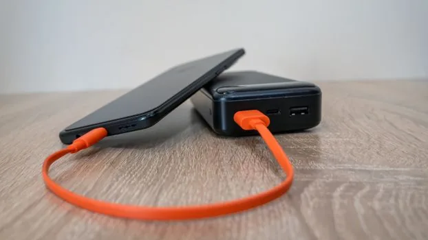 Galaxy smartphone connected to charger on desk with battery percentage visible, Korean home office, realistic photography