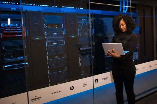 IT administrator reviewing firmware update page and vendor security statement for conference room equipment, laptop and printed checklist, realistic office | 화상회의 장비 펌웨어와 보안 문서를 점검하는 장면