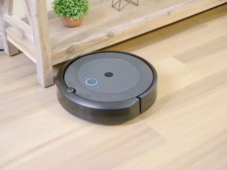 Korean user checking robot vacuum app permissions and home map data on a smartphone beside a charging robot vacuum, realistic editorial photo, bright clean home