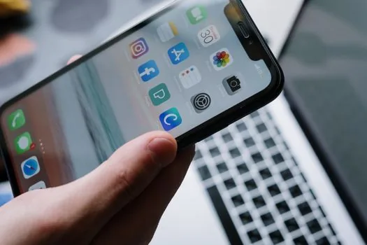 Korean user reviewing app notification permissions and email receipt settings on phone, laptop stock chart blurred in background, editorial realistic photo