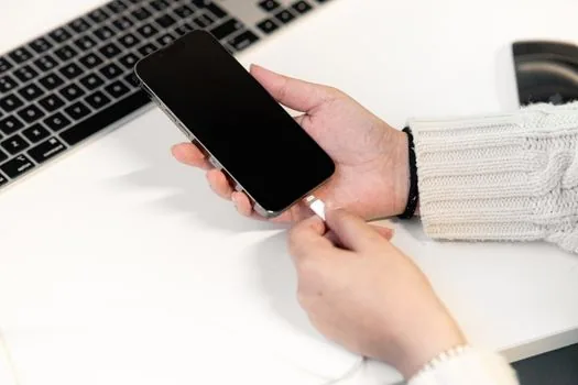 person checking iPhone optimized battery charging notification on lock screen beside cable and notebook, realistic bright desk photo | 최적화된 배터리 충전 알림을 확인하는 장면