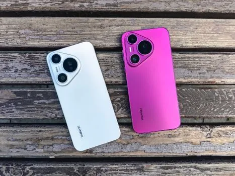 two Android phones charging side by side on a wooden desk, one showing battery settings concept, realistic editorial photo