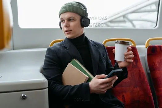 Commuter checking audio output picker on smartphone while wearing wireless earbuds inside a quiet bus, realistic photo | 조용한 버스 안에서 무선이어폰을 낀 이용자가 스마트폰 오디오 출력 선택을 확인하는 장면