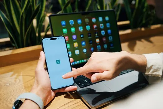 person holding compact foldable phone closed in one hand and open on table beside laptop, comparing pocket use and tablet use, realistic tech lifestyle photo